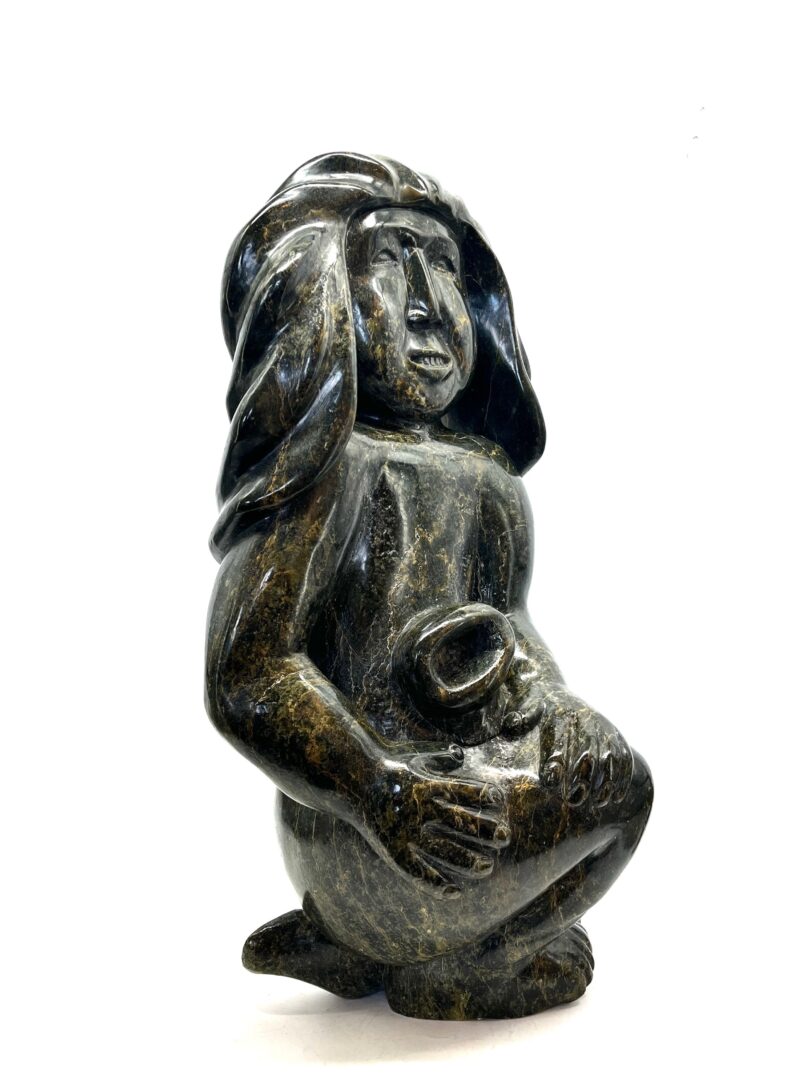 One original hand-carved sculpture by Inuit artist, Kaka Ashoona. Crouching figure sculpture made out of serpentine.