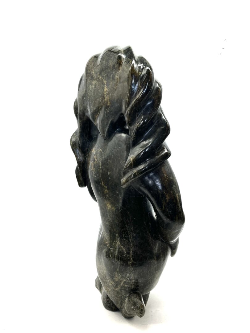 One original hand-carved sculpture by Inuit artist, Kaka Ashoona. Crouching figure sculpture made out of serpentine.