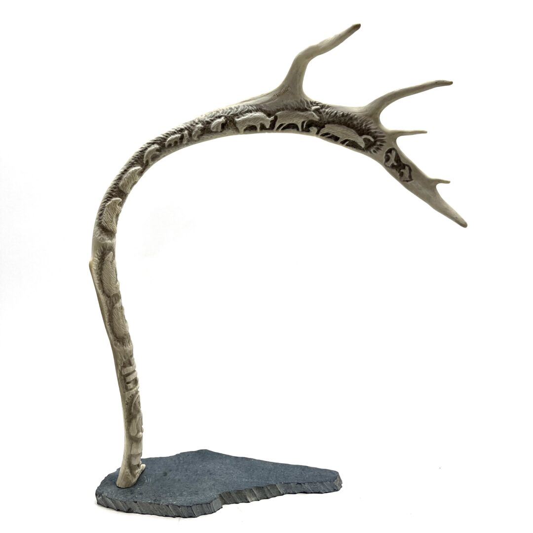 One original hand-carved sculpture by Inuit artist, Annie Angotialik. One caribou scene carved out of caribou antler and basalt.